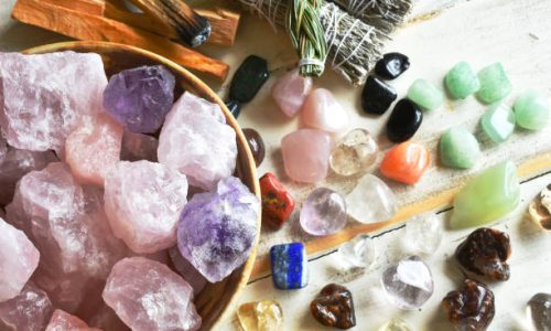 A top view image of a bowl of rose quartz crystals with several other healing crystal and smudge sticks.